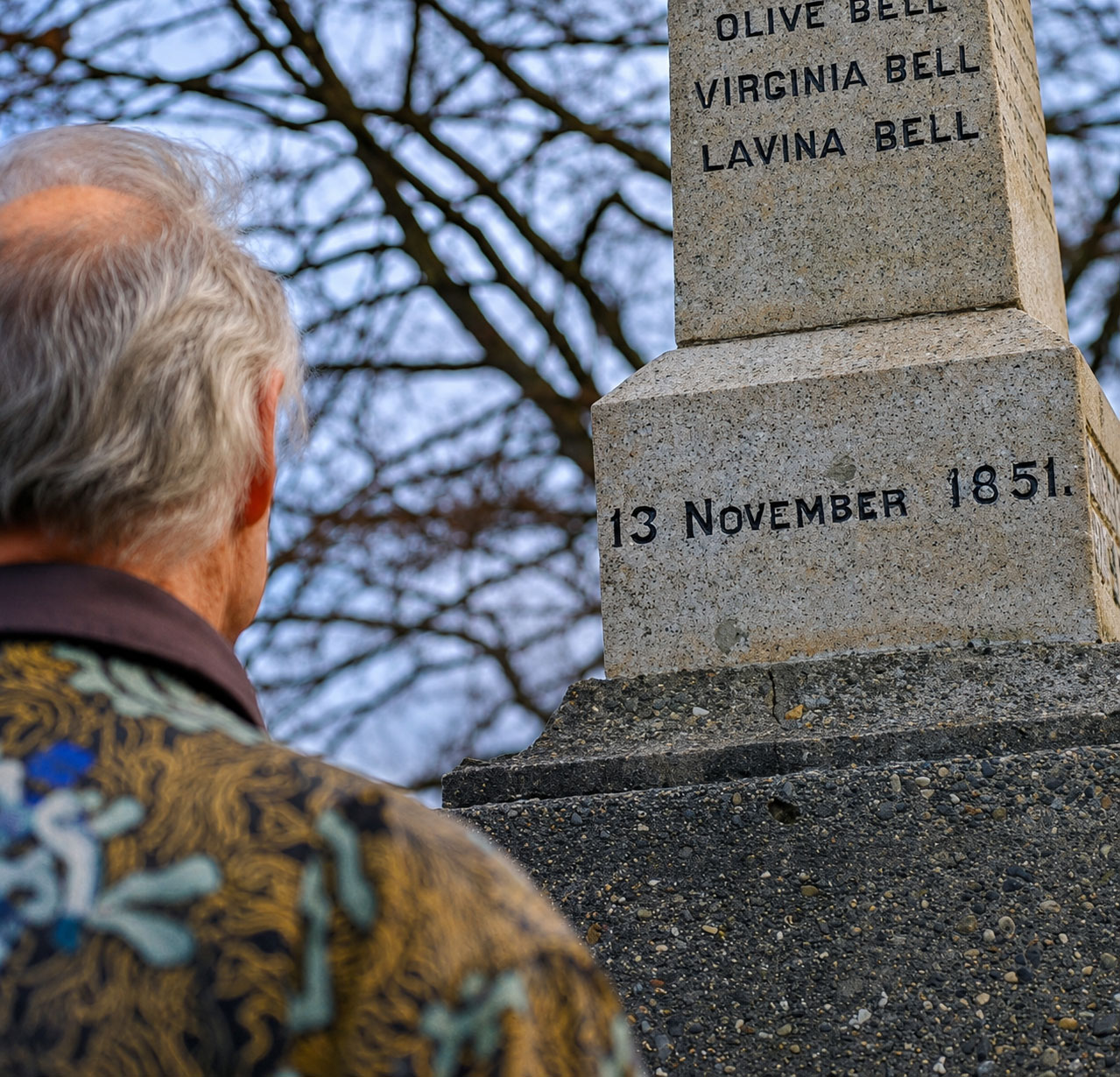 A person stands before a historic stone marker bearing the names of early settlers, November 13, 1851